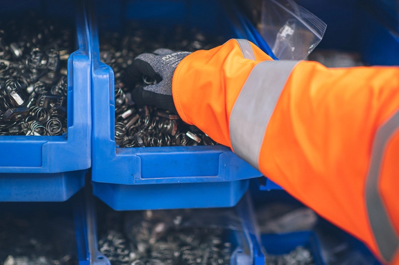 Man in a high vis picking up bolts from a blue tray