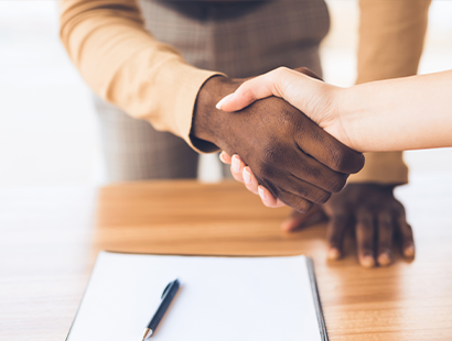 Two people shaking hands above a desk with paper and a pen on it