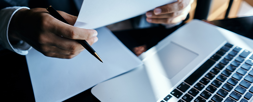 Business man in front of a laptop holding paper with a pen in his hand